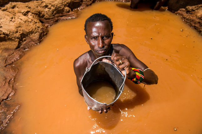 Leparkeri. a Samburu warrior, stands inside a well he has dug along a dry river bed where he will water his livestock during the dry season. They sing as they lift the buckets of water from the deep wells  and each warrior's cattle knows who his owner is