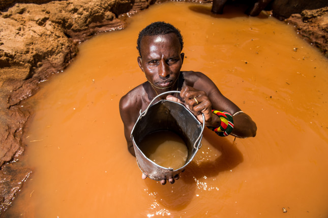 Leparkeri. a Samburu warrior, stands inside a well he has dug along a dry river bed where he will water his livestock during the dry season. They sing as they lift the buckets of water from the deep wells  and each warrior's cattle knows who his owner is