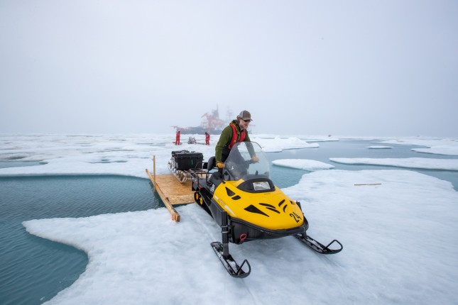 Matthew Shupe drives a snowmobile over a bridge towards MET City.